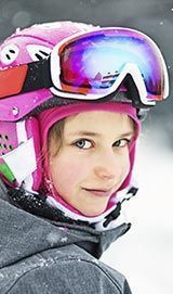 Glückliches kleines Mädchen auf dem Schnee mit Skihelm